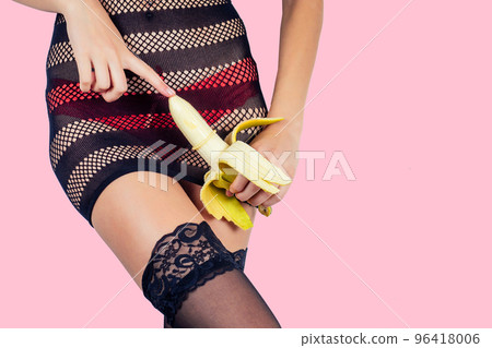 Closeup of a sexy woman body in red panties and black sexy transparent dress stockings touching a banana in a condom on pink background in the studio. intimate massage games cock safe sex Closeup of a sexy woman body in red panties and black sexy transparent dress stockings touching a banana in a condom on pink background in the studio. intimate massage games cock safe sex 96418006
