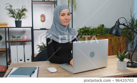 Young muslim business woman girl opens laptop start working makes online purchases, sends messages 96420703