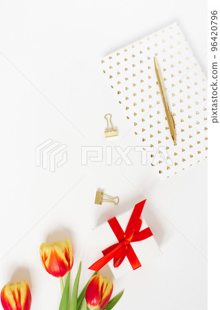 Feminine composition of women's work space, gifts for Mother's Day and Valentine's Day. A gift with a red ribbon and a bouquet of tulip flowers, a notebook and a pen. Flat lay and top view Feminine composition of women's work space, gifts for Mother's Day and Valentine's Day. A gift with a red ribbon and a bouquet of tulip flowers, a notebook and a pen. Flat lay and top view 96420796