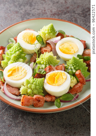 Salad Romanesco cauliflower buds with boiled eggs, red onion and bacon closeup on the plate. Vertical 96422571