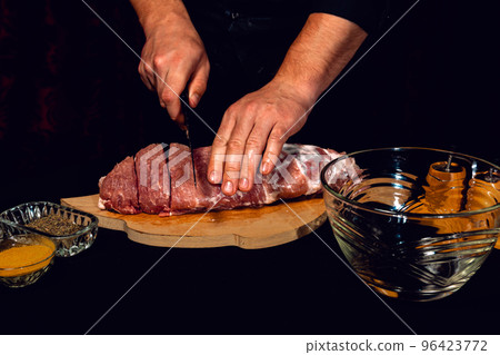 A man on a wooden board cuts pork into large pieces, close-up shows how to cut pork neck on a barbecue. 96423772