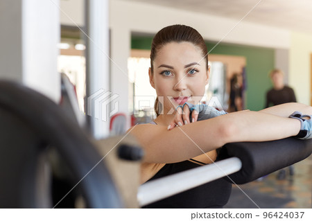 Portrait of confident young woman standing in gym. Athletic female looking at camera, being photographed by her friend while taking breather, works out in gymnasium. Healthy and sport lifestyle. 96424037