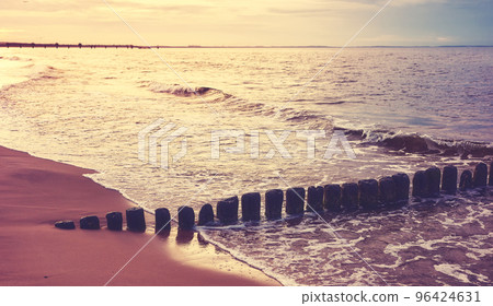 Wooden breakwater at a beach at sunset, selective focus, color toning applied. 96424631