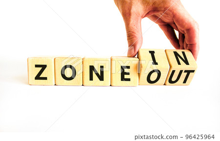 Zone in or out symbol. Concept words Zone in and Zone out on wooden cubes. Beautiful white table white background. Businessman hand. Business zone in or out concept. Copy space. 96425964