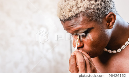 African transgender man putting on makeup on his eyes. 96426162