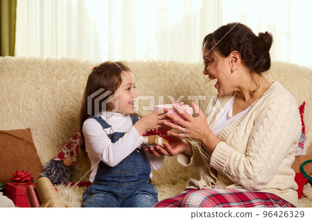 Happy multi-ethnic family of a loving mother and her lovely daughter, exchanging presents at Christmas, in cozy home interior. Magical festive atmosphere of winter holidays. Love. Family relationships Happy multi-ethnic family of a loving mother and her lovely daughter, exchanging presents at Christmas, in cozy home interior. Magical festive atmosphere of winter holidays. Love. Family relationships 96426329