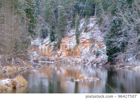 View of red sandstone cliffs. Salaca river. Skanaiskalns nature park. November is the first snow in Mazsalaca in Latvia. 96427507