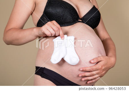 Pregnant woman with a bare stomach and a small child's socks in hands 96428053