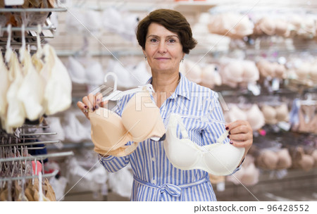 Mature woman considering brassiere in Underwear section of the supermarket Mature woman considering brassiere in Underwear section of the supermarket 96428552