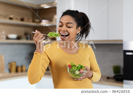 Portrait of cheerful young black pregnant woman with big belly eating salad with organic vegetables Portrait of cheerful young black pregnant woman with big belly eating salad with organic vegetables 96428858