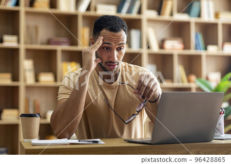 Sad tired arab male freelancer working on laptop and touching head, holding glasses, looking at computer screen Sad tired arab male freelancer working on laptop and touching head, holding glasses, looking at computer screen 96428865