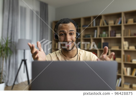 Happy arab man in headphones having video call on laptop, talking and gesturing at computer webcamera in home office Happy arab man in headphones having video call on laptop, talking and gesturing at computer webcamera in home office 96428875