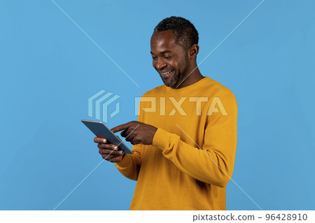 Cheerful black man using digital tablet isolated on blue Cheerful black man using digital tablet isolated on blue 96428910