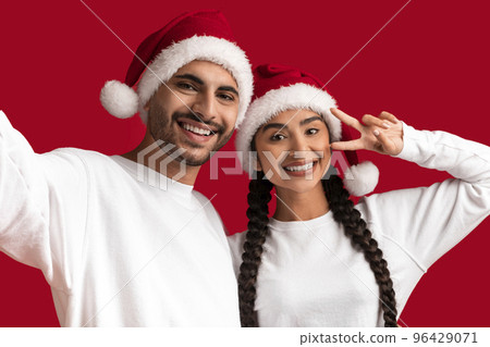 Happy Young Middle Eastern Couple In Santa Hats Taking Selfie Together Happy Young Middle Eastern Couple In Santa Hats Taking Selfie Together 96429071
