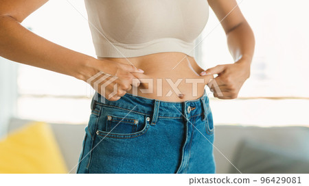 Young woman in jeans pinching fat of her abdomen zone, ready for slimming or liposuction treatment, panorama, cropped 96429081