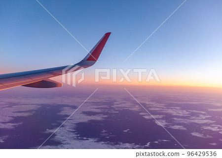 Airplane flight at sunset or dawn. Aircraft's wing and land seen through the illuminator. View from the window of the plane. Airplane, Aircraft. Traveling by air. Airplane flight at sunset or dawn. Aircraft's wing and land seen through the illuminator. View from the window of the plane. Airplane, Aircraft. Traveling by air. 96429536