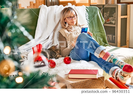 Christmas holiday online shopping at home. Happy blond woman buying holiday gifts using smartphone for searching promotion on Black Friday or cyber Monday. 96430351