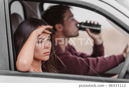Drunk driving couple upset tired from drinking in car. Man driver holding beer beverage at the steering wheel, angry Asian woman girlfriend drowsy. 96433112
