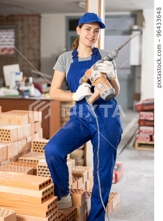 Female builder in blue workwear standing with demolition hammer Female builder in blue workwear standing with demolition hammer 96433648