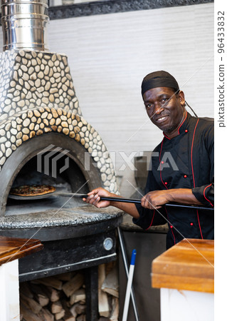 Portrait of african american chef man baking pizza in oven Portrait of african american chef man baking pizza in oven 96433832