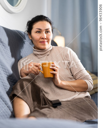 Woman holding cup of coffee and watching TV at home Woman holding cup of coffee and watching TV at home 96433906