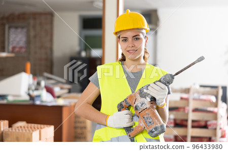 Young female builder standing with demolition hammer Young female builder standing with demolition hammer 96433980