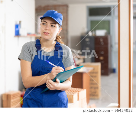 Female contractor checking blueprints and taking notes at building site Female contractor checking blueprints and taking notes at building site 96434032