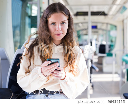 Portrait of a positive girl on public transport and texting on a mobile phone Portrait of a positive girl on public transport and texting on a mobile phone 96434135