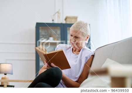attractive elderly woman reading a book in her living room. 96439930