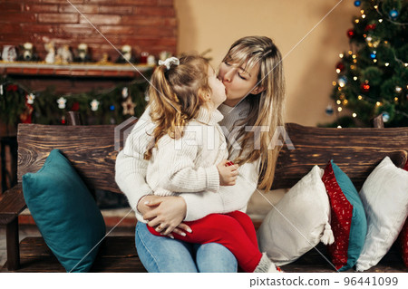 Happy mom and baby daughter reading having fun by the fireplace on Christmas or New Year's Eve. Parenthood, childhood, time together, holidays Happy mom and baby daughter reading having fun by the fireplace on Christmas or New Year's Eve. Parenthood, childhood, time together, holidays 96441099