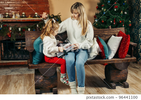 Cute mom and daughter are looking through a family photo album on Christmas Eve, spending time together by the fireplace and the Christmas tree. Christmas, New Year, memories, family evening Cute mom and daughter are looking through a family photo album on Christmas Eve, spending time together by the fireplace and the Christmas tree. Christmas, New Year, memories, family evening 96441100