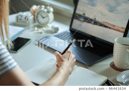 Freelancer working at home office. Woman using laptop and writing in notepad sitting at table in home office 96441634