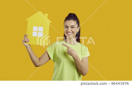 Studio portrait of happy young woman smiling and pointing at paper house in her hand 96443976
