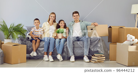 Happy young family with children sitting on sofa between cardboard boxes in their new apartment. 96444212