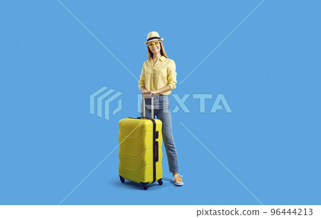 Happy tourist girl standing with her yellow suitcase against blue studio background Happy tourist girl standing with her yellow suitcase against blue studio background 96444213