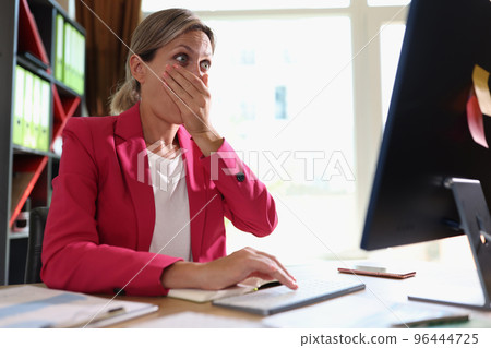Surprised woman sitting at workplace and looking at computer display 96444725