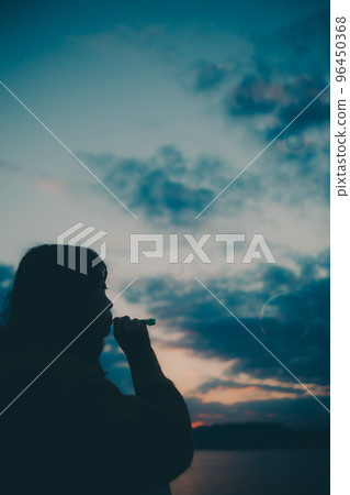 Silhouette photo of a young woman sitting and blowing bubbles Silhouette photo of a young woman sitting and blowing bubbles 96450368