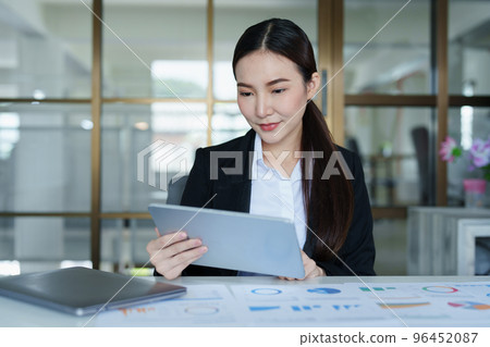Portrait of a thoughtful Asian businesswoman looking at financial statements and making marketing plans using a tablet computer on her desk. Portrait of a thoughtful Asian businesswoman looking at financial statements and making marketing plans using a tablet computer on her desk. 96452087