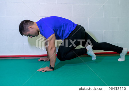 Young muscular male athlete trains mountain climbing ground exercise. Background with blank wall, copy space. 96452530