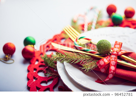Christmas festive table setting with white plates and gold cutlery, red linen napkin, fir branches, red and green balls Christmas festive table setting with white plates and gold cutlery, red linen napkin, fir branches, red and green balls 96452781