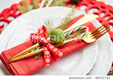 Christmas festive table setting with white plates and gold cutlery, red linen napkin, fir branches, red and green balls Christmas festive table setting with white plates and gold cutlery, red linen napkin, fir branches, red and green balls 96452782