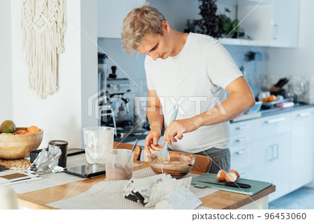 Young man cooking brownie cake on the light modern kitchen at home. Preparing steps for baking cake. Culinary hobby. Cooking online video classes on smartphone. Selective focus. copy space. Young man cooking brownie cake on the light modern kitchen at home. Preparing steps for baking cake. Culinary hobby. Cooking online video classes on smartphone. Selective focus. copy space. 96453060