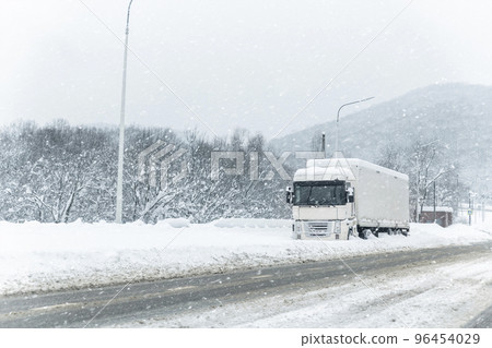 Big commercial semi-trailer truck trapped in snow drift on closed highway road at heavy snow storm blizzard cold winter day. Cargo vehicle stuck on freeway at bad weather conditions frosty snowfall 96454029