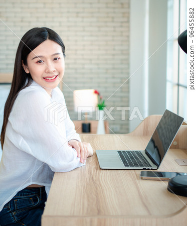 Happy beautiful asian woman working on a laptop at the home office sitting at table. Happy female professional freelancer online using notebook pc concept. 96455882