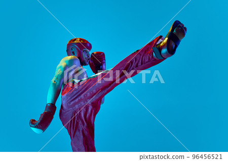 Workout of professional athlete. Kickboxer in helmet and gloves training isolated over blue background in neon light. Muay thai. Sport, competition, energy, combat sports Workout of professional athlete. Kickboxer in helmet and gloves training isolated over blue background in neon light. Muay thai. Sport, competition, energy, combat sports 96456521