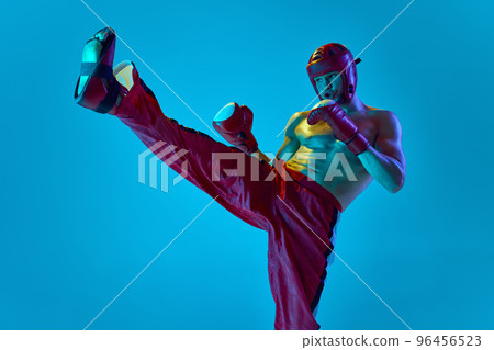 Workout of professional athlete. Kickboxer in helmet and gloves training isolated over blue background in neon light. Muay thai. Sport, competition, energy, combat sports Workout of professional athlete. Kickboxer in helmet and gloves training isolated over blue background in neon light. Muay thai. Sport, competition, energy, combat sports 96456523