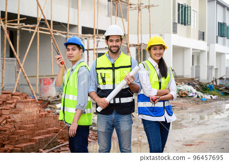 Group of happy contractors, engineers and formats in safety vests with helmets stand on the under-construction building site. teamwork concept. Group of happy contractors, engineers and formats in safety vests with helmets stand on the under-construction building site. teamwork concept. 96457695