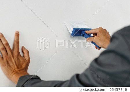man spreading some glue on a wall 96457846