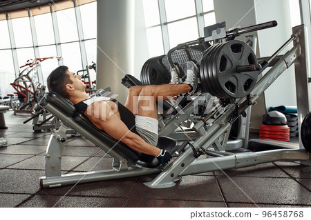 Man Using A Press Machine In A Fitness Club. Strong man doing an exercise on its feet in the simulator. Side view. 96458768