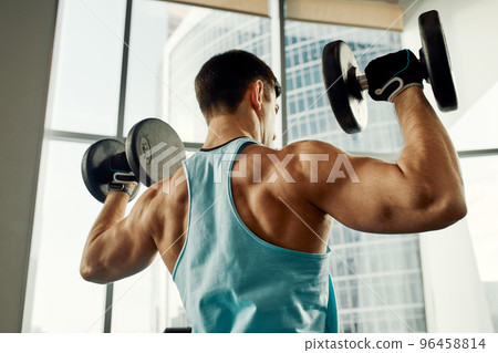 Man doing exercise with dumbbell leaning on sports bench in the gym. Photo of a sexy muscular man in sportswear and good physique on grey background. Strength and motivation, sport, fitness goal Man doing exercise with dumbbell leaning on sports bench in the gym. Photo of a sexy muscular man in sportswear and good physique on grey background. Strength and motivation, sport, fitness goal 96458814